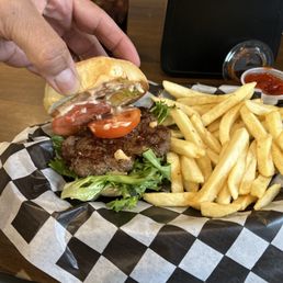 A burger with tomato slices, lettuce, and a beef patty, served with French fries and ketchup in the background.