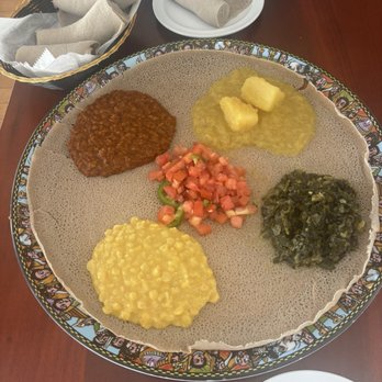 Ethiopic - Trying Ethiopian food for the first time! - Ethiopian cuisine featuring a large round injera bread with multiple toppings including lentils, vegetables, and stews, accompanied by bread rolls and a basket of bread. - Ethiopian Near Me - Washington, DC, District of Columbia