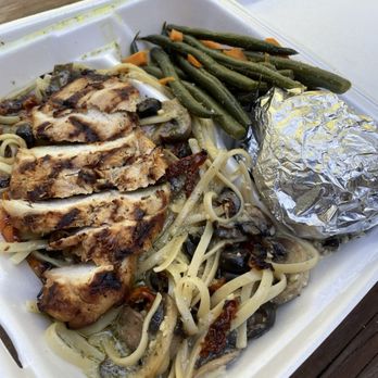 Kalamata - Mediterranean Chicken Pasta. IG: @bayareapineapples - A foam takeout container holds grilled chicken slices, pasta with vegetables such as mushrooms and sun-dried tomatoes, green beans with carrots, and a foil-wrapped baked potato. The food appears freshly prepared and is served in a disposable container, placed on a wooden surface. - Mediterranean Near Me - Arnold, California