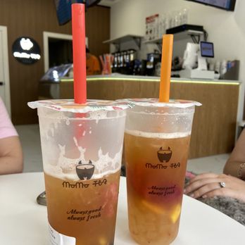 MoMo Tea - Two bubble tea drinks with colorful straws are placed on a table inside MoMo Tea, a bubble tea store with a space-themed interior and digital menu screens. - Bubble Tea Near Me - Bellmore, New York