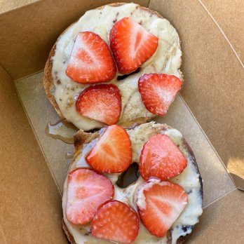 Oromo Cafe - Strawberry Cashew Cream Bagel - A close-up of two bagel halves topped with cream cheese, fresh sliced strawberries, and a drizzle of honey, placed inside a brown cardboard takeout box. The bagels appear toasted, and the strawberries are arranged on top, adding color and freshness to the dish. - Coffee & Tea Near Me - Chicago, Illinois
