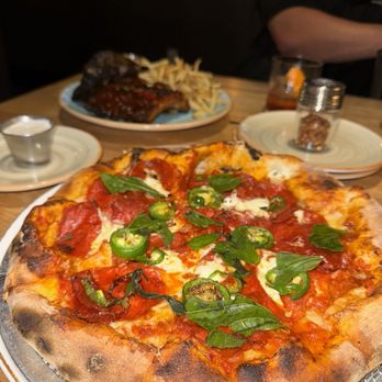 Cork & Pig Tavern - Ultimate pepperoni pizza with fresh jalapeños and bone in Texas Pork Back Ribs in the background. - New American Near Me - Odessa, Texas