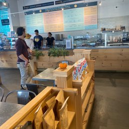 Inside - Inside a cafe, customers are placing orders at a counter with a large menu board overhead, featuring various food and drink options.