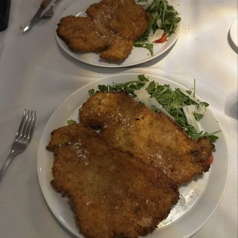 Laboratorio Kitchen - Two plates of breaded fried fish served with side salads of greens and shaved cheese, on a white table at a restaurant. - New American Near Me - Montclair, New Jersey