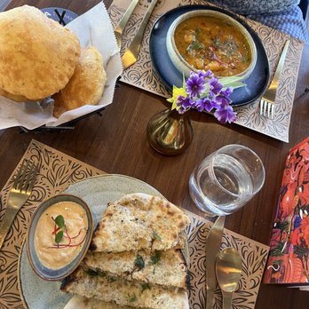 Tamashaa - Potato curry & potato cauliflower kulcha - The image shows a table with Indian cuisine, including naan bread, a bowl of curry, and fried snacks, with utensils, a glass of water, and a small flower vase. - Indian Near Me - Washington, DC, District of Columbia