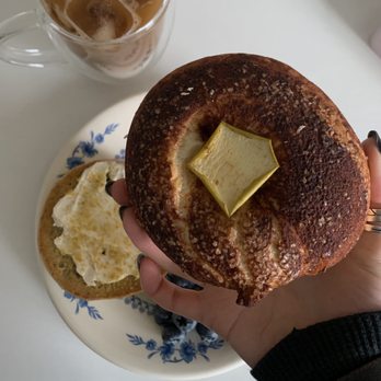 The Daily Bagel - a person holding a bagel with butter on it - Bagels Near Me - Eugene, Oregon The Daily Bagel - a person holding a bagel with butter on it - Bagels Near Me - Eugene, Oregon