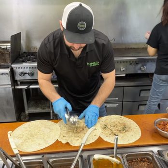 Bubbakoo's Burritos - A man wearing a black polo shirt, blue gloves, and a black and white cap is preparing burritos in a kitchen at Bubbakoo's Burritos. - Mexican Near Me - Mount Olive, New Jersey