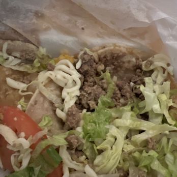 El Coyote - Beef taco dinner - A taco with ground beef, shredded lettuce, tomato slices, and shredded cheese inside a soft flour tortilla. The taco appears partially eaten, with some paper wrapping visible in the background. The ingredients are fresh and typical of Mexican-style tacos. - Mexican Near Me - Alsip, Illinois
