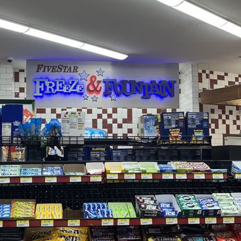 Five Star Shell - Interior - The image shows the interior of a convenience store with a prominent sign reading 'Fivestar Freeze & Fountain' in blue and red neon lights on the wall. The ceiling has fluorescent lighting, and the wall behind the sign features white tiles with red accents. Shelves below the sign display various snack items, ice packs, and frozen products. The store appears well-lit and organized, with a focus on the beverage and snack sections. - Grocery Near Me - Frankfort, Kentucky
