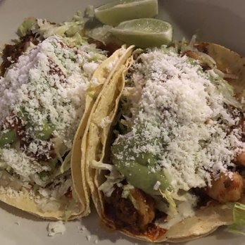 El Torero - Shrimp and chorizo tacos - Two tacos filled with seasoned meat, shredded lettuce, and cheese, topped with shredded cheese and a green sauce, served with lime wedges on a white plate. The tacos are made with soft corn tortillas and garnished with shredded cheese and lime slices, typical of Mexican cuisine. - Mexican Near Me - Tucson, Arizona