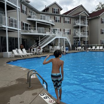 Delavan Lake Resort - A boy in striped swim trunks stands at the pool's edge, overlooking the water at a resort with multiple balconies and lounge chairs. - Resorts Near Me - Delavan, Wisconsin