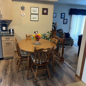 Build Right 518 - A round wooden dining table with six matching chairs, decorated with a Mickey Mouse-themed fruit centerpiece, is situated in a dining area near a kitchen. - General Contractors Near Me