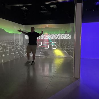 Electric Playhouse - A person is posing in front of an interactive digital game display with a high score of 256, in a dark indoor setting with colorful lighting. - Party & Event Planning Near Me - Albuquerque, New Mexico