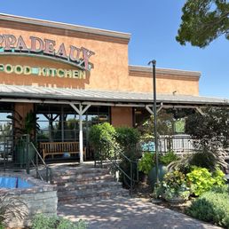 Entry - The image shows the storefront of Pappadeaux Seafood Kitchen, featuring a large sign, outdoor seating, and surrounding greenery.