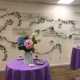 Par-tea @Green Apron Kitchen - Tea party display with purple tablecloths, floral centerpieces, and wall decor featuring quotes and greenery.