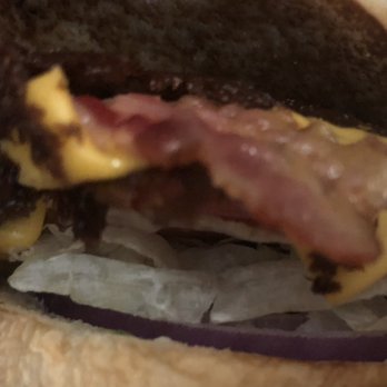 Culver's - A close-up image of a burger featuring crispy bacon, melted cheese, sliced red onions, and a toasted bun. The burger is partially wrapped in white paper, with some ingredients visible from the side view. - Burgers Near Me - Ottawa, Illinois