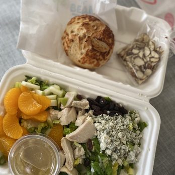 Bubble N Bean - Pasadena Bleu Salad - A takeout salad includes orange slices, chopped chicken, blue cheese, greens, and dried cranberries, with a small cup of dressing, along with a roll and a bag of nuts. - Coffee & Tea Near Me - Draper, Utah