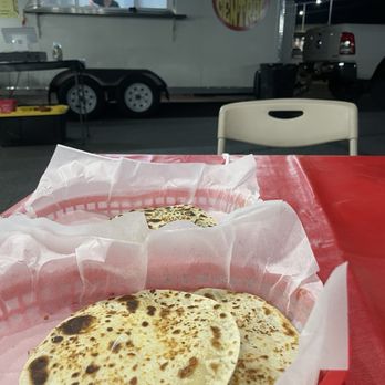 Taco Central - Cheese Quesadillas - Two quesadillas are served in paper baskets on a red plastic table at an outdoor dining area. The background features a food truck with a window and a person inside, along with parked vehicles and a night sky. The scene suggests a casual outdoor meal at a food truck location. - Tacos Near Me - Phoenix, Arizona