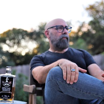 Old Humble Distilling Company - a man sitting in a chair with a glass of whiskey - Distilleries Near Me - Humble, Texas Old Humble Distilling Company - a man sitting in a chair with a glass of whiskey - Distilleries Near Me - Humble, Texas