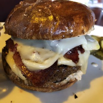 Irish Times - Reuben burger!! - A close-up image of a burger with a toasted brioche bun, melted cheese, and crispy bacon. The burger appears to be served on a plate in a restaurant setting, with some background elements visible. The burger looks hearty and well-prepared, with the cheese melted over the patty and bacon slices visible inside. - Pubs Near Me - Brookfield, Illinois