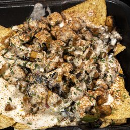 a plate of nachos - A seafood dish with a creamy sauce, topped with chopped herbs, served over crispy chips in a black container.