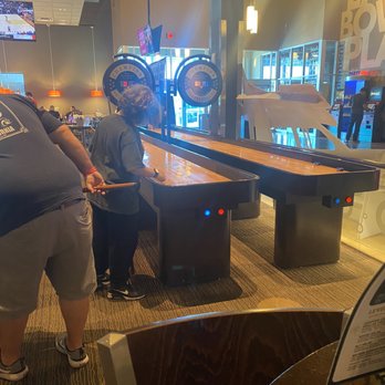 Main Event Gilbert - Two individuals are engaged in a game of air hockey at an arcade within a family entertainment venue, with multiple screens and arcade machines visible. - Bowling Near Me - Gilbert, Arizona