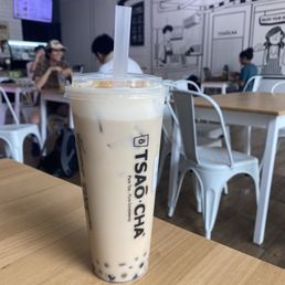 Caramel Cloud Black Milk Tea - A large plastic cup of caramel cloud black milk tea with tapioca pearls is placed on a wooden table inside Tsaocaa, a bubble tea shop in Austin, TX.