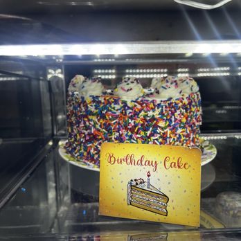 Bettola - Ingenious!!  How many times do we take someone for a birthday dinner and forget or can't bring the cake??!!! - A birthday cake covered in multicolored sprinkles and topped with whipped cream dollops, displayed in a glass case with a birthday card. - Pizza Near Me - Cranston, Rhode Island