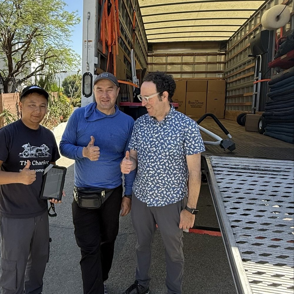 Two movers and a customer standing in front of a moving truck holding thumbs up. Two movers and a customer standing in front of a moving truck holding thumbs up.