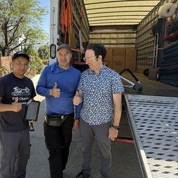Two movers and a customer standing in front of a moving truck holding thumbs up.