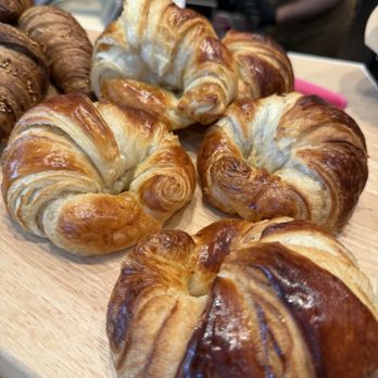 Crepe Therapy Cafe - A close-up of golden-brown croissants on a wooden board, with other baked goods visible in the background. - Creperies Near Me - Boulder, Colorado