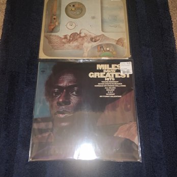 Dusty Groove - Two vinyl records in protective plastic sleeves are laid on a dark blue textured surface, with visible price tags on each. - Music & DVDs Near Me - Chicago, Illinois