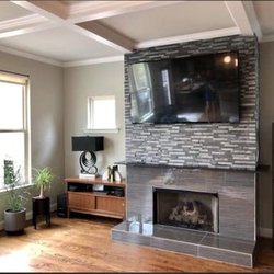 Perfect Remodeling - This inviting living room features a modern fireplace with a grey tiled surround and ledger stone accent wall, topped by a mo...