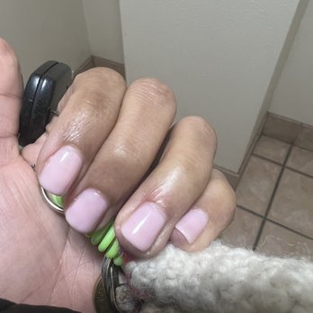 Chippen Nails Edwards - Nails - The image shows a hand with well-groomed, light pink painted nails gripping a set of keys. A small, curly-haired dog is partially visible at the bottom of the frame, with its head and part of its body shown. The background includes a tiled floor and a plain wall, suggesting an indoor setting. - Nail Salons Near Me - Edwards, Colorado