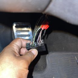 Loose wires attached to harness - A hand is holding a wiring harness with multiple colored wires, some with red connectors, inside a vehicle near the footwell area.