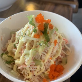 Nori Restaurant - Kani Salad - A crab salad served in a white bowl, topped with chopped green onions, orange fish roe, and a drizzle of mayonnaise, on a wooden table. - Asian Fusion Near Me - St. Augustine, Florida