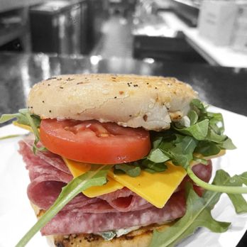 Bushwick - A sandwich featuring tomato slices, arugula, cheddar cheese, and various meats on a toasted bun, served on a white plate. - Tacos Near Me - Warren, Ohio