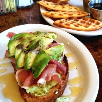 Toast - Foreground: Prosciutto, ricotta and honey toast with added avocado ($5 plus avocado). Background: Waffles with maple syrup and butter ($6). - Breakfast & Brunch Near Me - New Orleans, Louisiana