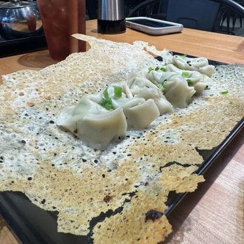 Dough Zone Dumpling House - Fried gyoza - Dumplings garnished with green onions are presented on a large, crispy rice cracker on a black tray, with drinks and condiments on the table. - Chinese Near Me - Berkeley, California