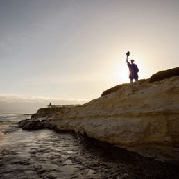 Standing overhead holding a cap above, perfectly blocking the sun. Creating a beautiful shadow.