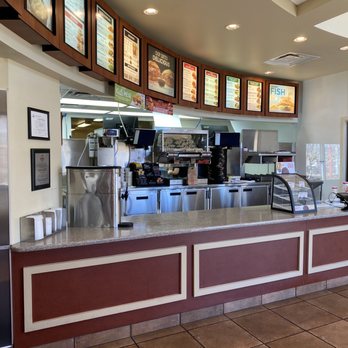 Arby's - Ordering counter. - A fast-food restaurant counter with digital menu screens displaying food options, coffee machines, and a door to the kitchen area. - Sandwiches Near Me - Santa Fe, New Mexico
