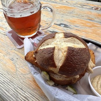 Notch Brewing - A glass mug of beer and a large sandwich with a pretzel bun are placed on a wooden table outdoors. - Breweries Near Me - Salem, Massachusetts