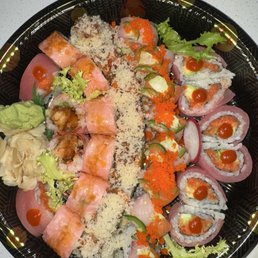 J14. Fantastic Roll E27. Crunch Roll J24. Victoria Secret Roll J17. Sweet Heart Roll (left to right) - A large black sushi platter contains multiple types of sushi rolls topped with fish, fish roe, and sauces, accompanied by wasabi and pickled ginger.