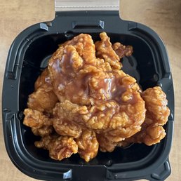 Honey BBQ - Fried chicken pieces coated in honey BBQ sauce are inside a black plastic takeout container.