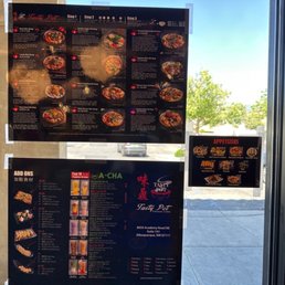 Menu - Three menus and an appetizer sign are attached to a glass door of Tasty Pot restaurant. The menus feature images and descriptions of different hot pot dishes, drinks, and add-ons. The background shows a parking lot with cars and trees outside, with clear weather and blue sky.