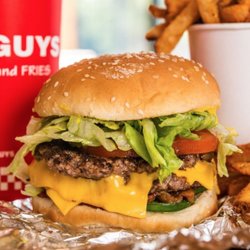 A close-up photograph of a Five Guys cheeseburger, soft drink in red Five Guys cup, and regular order of fries.