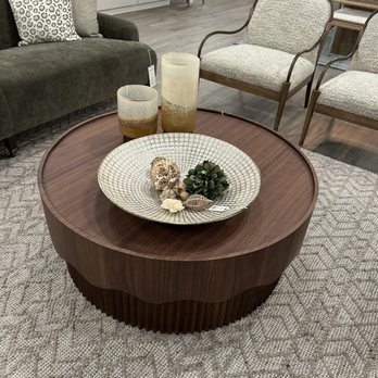 Hedi’s - A wooden coffee table with a decorative bowl, candles, and plants, situated in a furniture store setting with chairs and a sofa. - Furniture Stores Near Me - Chestnut Hill, Massachusetts