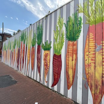 Calico - Carrot / beets mural - A mural featuring painted carrots is displayed on a wooden fence in an outdoor urban area with brick pavement and nearby buildings. - Cocktail Bars Near Me - Washington, DC, District of Columbia