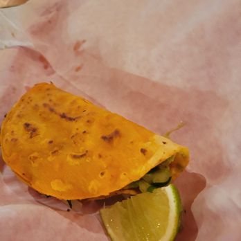 Sabor Tapatio - Birria taco - A taco with a yellow corn tortilla, filled with ingredients, served on pink paper, with a lime wedge on the side. - Food Trucks Near Me - Austin, Texas