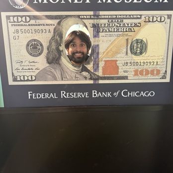 Money Museum - A person’s face appears through a hole in a large, fake hundred-dollar bill display at the Money Museum in Chicago, Illinois. - Museums Near Me - Chicago, Illinois